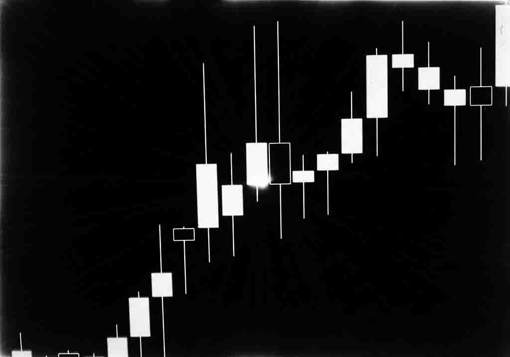 Eine schwarz-weiße, kontrastreiche Darstellung eines Finanz-Candlestick-Charts. Die Kerzenkörper sind helle (weiße) Rechtecke, die gegen einen tiefschwarzen Hintergrund mit leicht körnigen oder strahlenförmigen Rändern abgebildet sind.